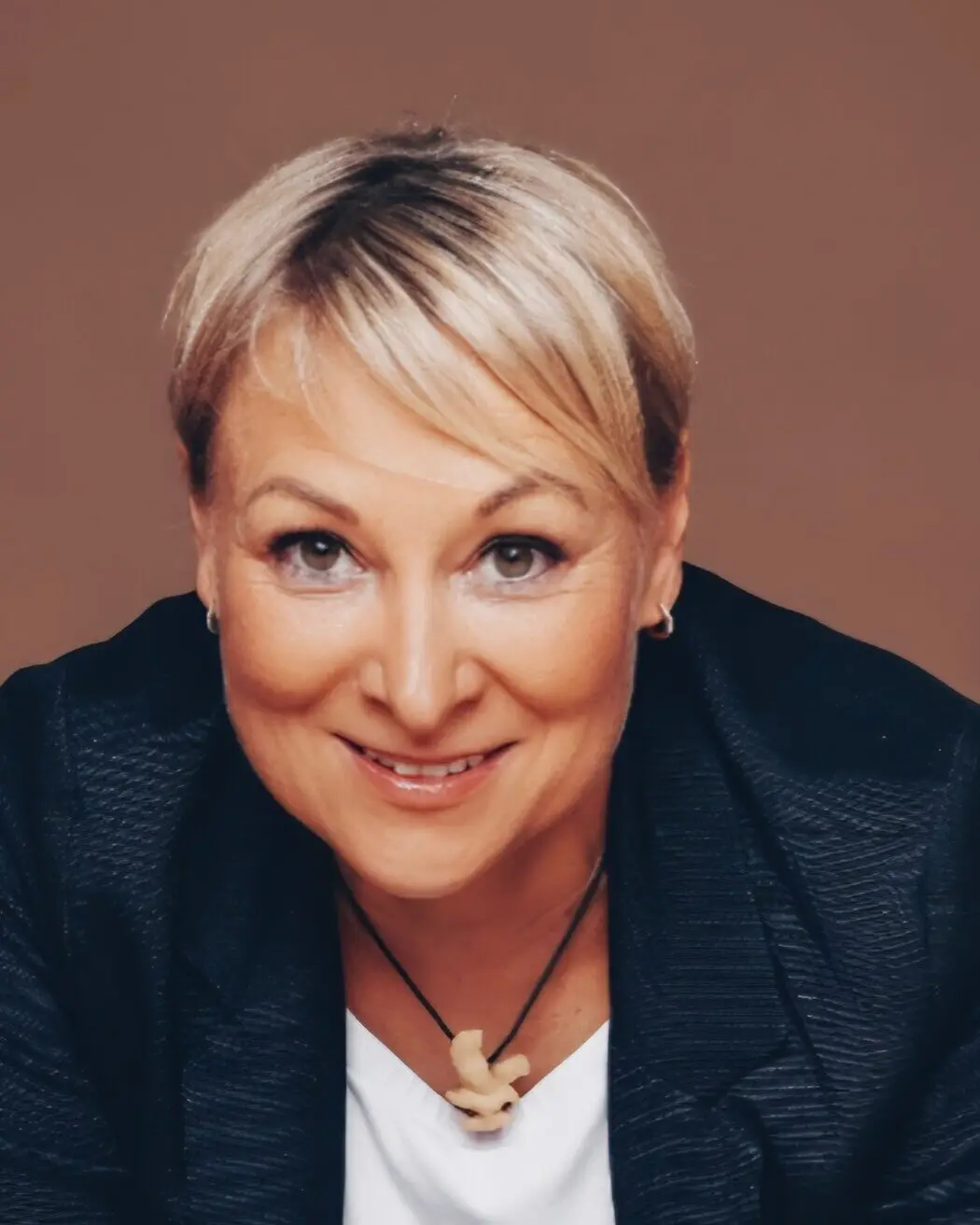 Heike Berndt im dunklen Blazer vor braunem Hintergrund, lächelnd in die Kamera